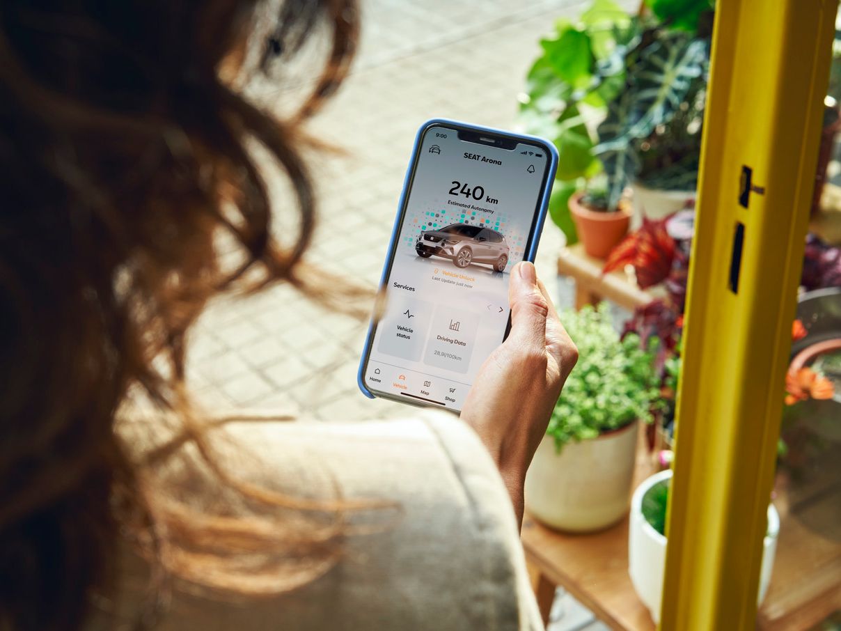 Eine Frau schaut auf ihr Smartphone und checkt die Reichweite von ihrem SEAT Arona.
