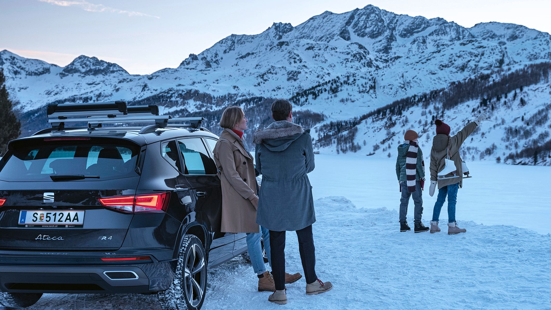 Eine Familie parkt mit ihrem schwarzen SEAT Ateca an einem zugefrorenen See in den winterlichen Bergen.