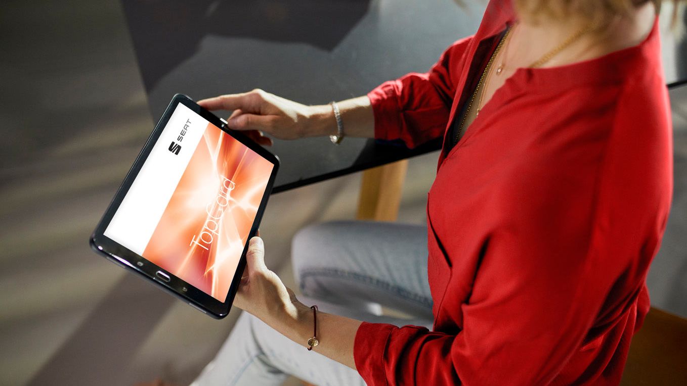 Eine Frau hält ein Tablet in der Hand, auf dem die SEAT TopCard sichtbar ist.