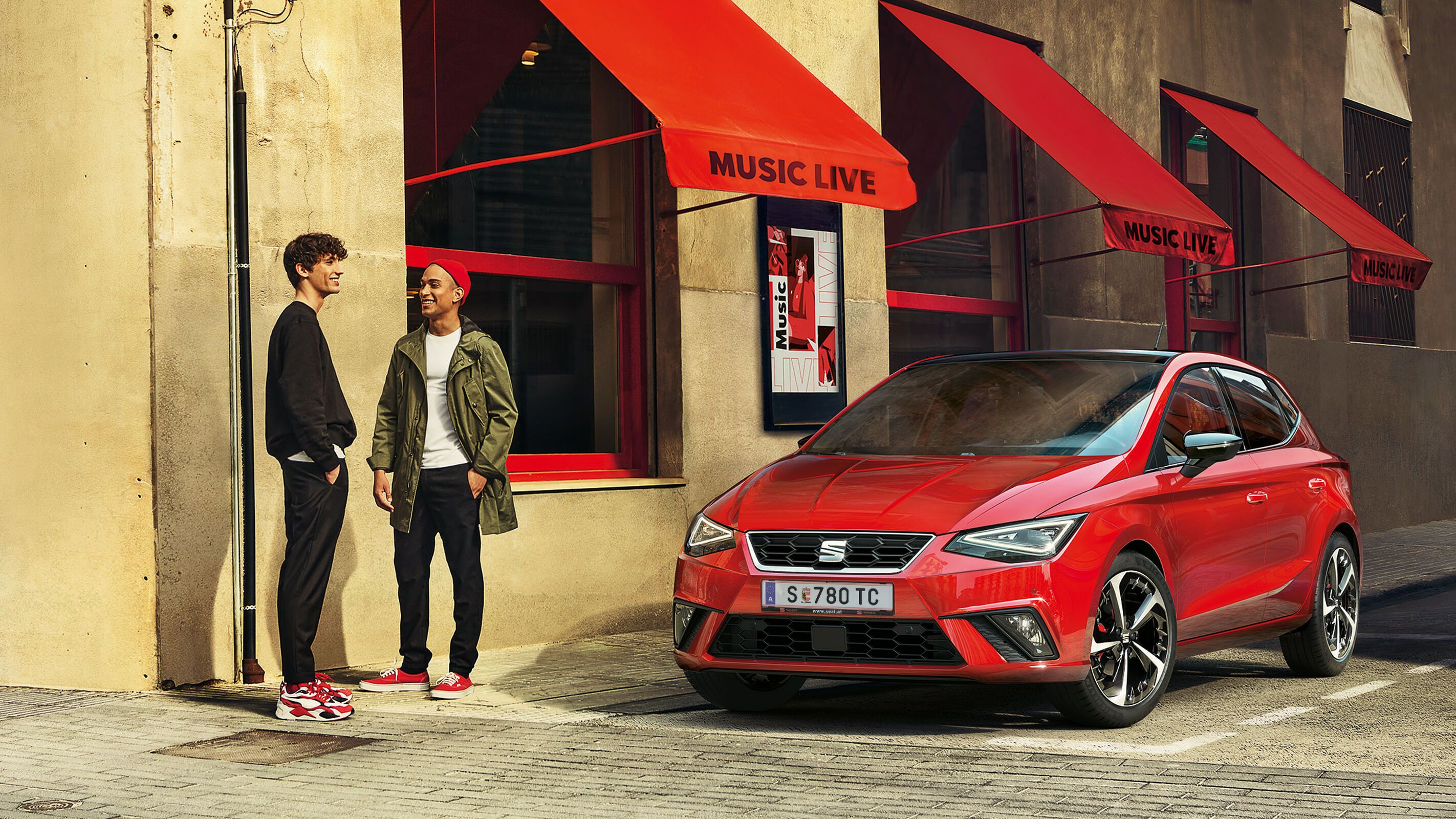 Ein roter SEAT Ibiza steht vor einem Gebäude während zwei Männer davor reden