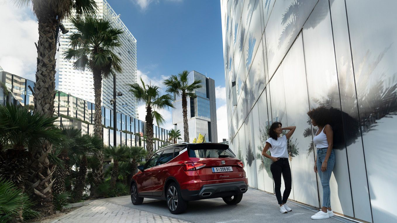 Ein roter SEAT Arona ist perspektivisch von hinten aufgenommen, während zwei Frauen daneben im Gespräch vertieft sind