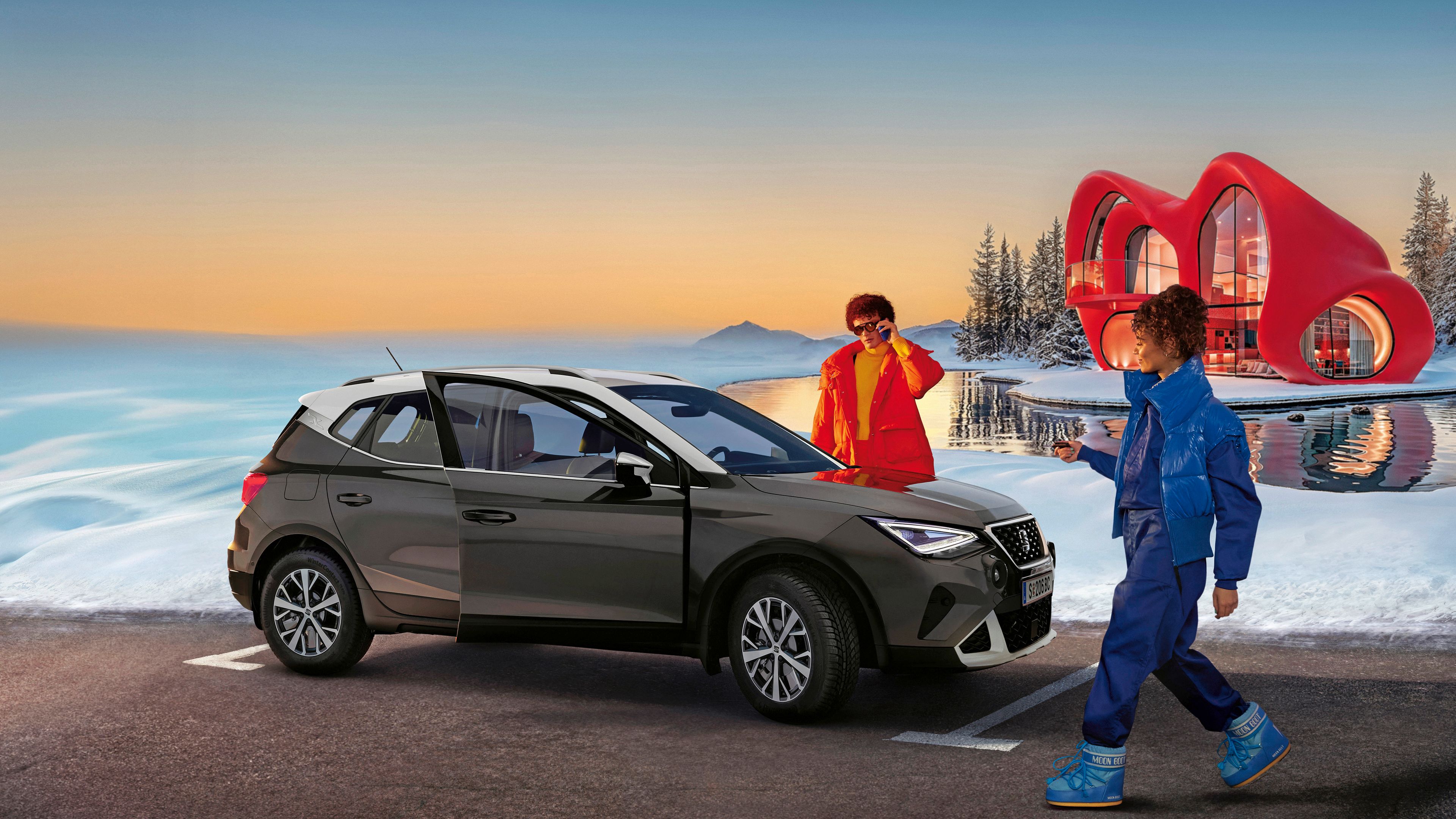 Ein SEAT Arona auf einem Parkplatz in einer verschneiten Landschaft. Ein Mann und eine Frau in Skianzügen bewegen sich um das Fahrzeug herum.