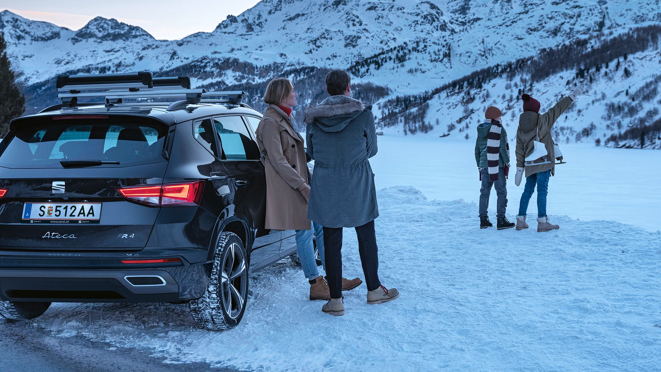 Eine Familie parkt mit ihrem schwarzen SEAT Ateca an einem zugefrorenen See in den winterlichen Bergen.